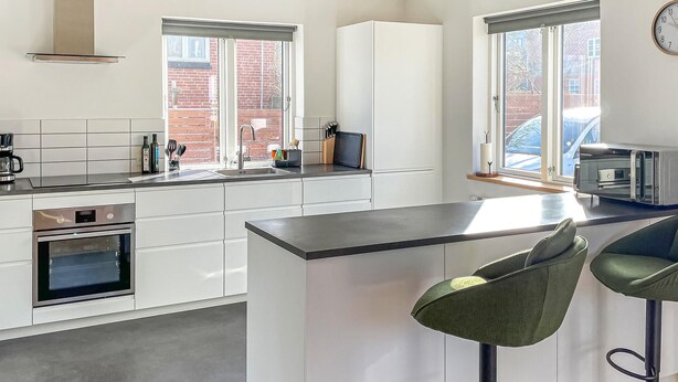 A modern kitchen with white cabinets, a built-in oven, a coffee machine, and a bar area with two green bar stools. - 2 bedroom awesome home in Faaborg (Faaborg)