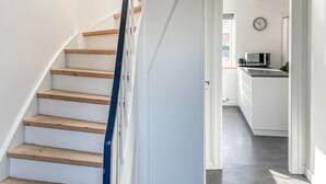 A staircase with wooden steps and a blue handrail, leading to a kitchen area with a microwave and a clock on the wall. - 2 bedroom awesome home in Faaborg (Faaborg)