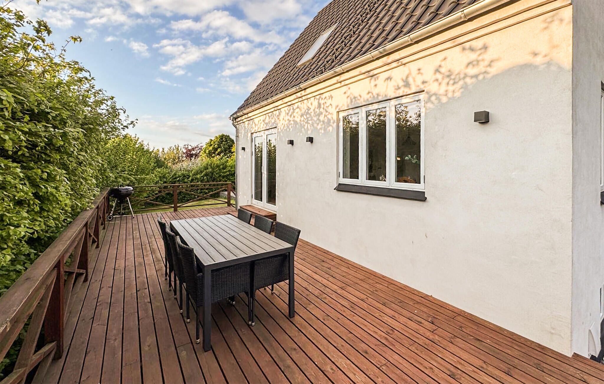 Une terrasse avec une table et des chaises, un barbecue et un bâtiment blanc doté de fenêtres.