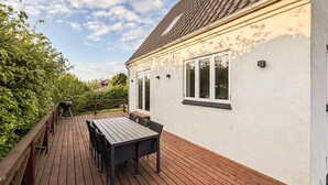 A deck with a table and chairs, a barbecue grill, and a white building with windows. - 2 bedroom awesome home in Faaborg (Faaborg)