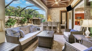 Une terrasse ensoleillée, meublée de mobilier en osier, avec un mur en pierre et une vue sur un jardin tropical.