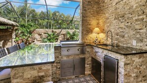 Une cuisine avec un mur en pierre, une table à plateau en verre, un évier et un four encastré.