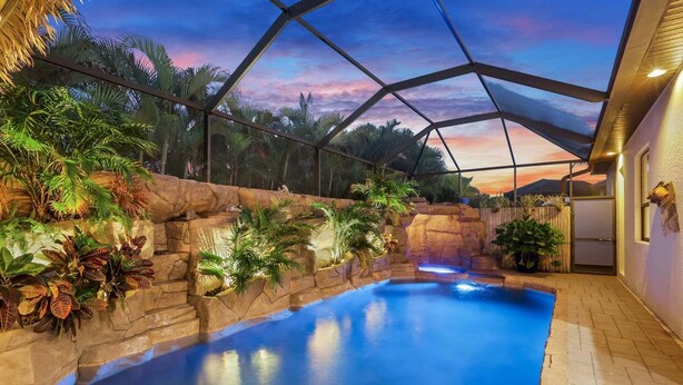 Une piscine intérieure dotée d’un mur d’escalade et de plantes tropicales, le tout sous une verrière offrant une vue sur le coucher de soleil.