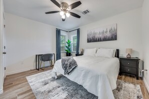 Ein Schlafzimmer mit Bett, Schreibtisch, Stuhl, Deckenventilator und einem Fenster mit Vorhängen.