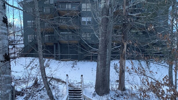 Un puente de madera sobre un sendero cubierto de nieve que lleva a un edificio con varios balcones.