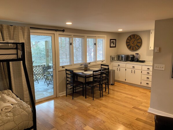A kitchen with a dining table, chairs, a clock, and a view through the glass door.