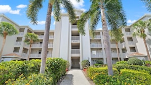 A multi-story hotel with a central entrance, surrounded by palm trees and well-maintained hedges. - Bonita Greens Retreat | Golf View Condo | Highland Woods | Near Bonita Beach (Bonita Springs)