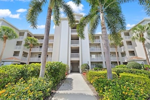 A multi-story hotel with a central entrance, surrounded by palm trees and well-maintained hedges. - Bonita Greens Retreat | Golf View Condo | Highland Woods | Near Bonita Beach (Bonita Springs)