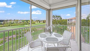 A balcony with a table and chairs, a ceiling fan, and a view of a golf course. - Bonita Greens Retreat | Golf View Condo | Highland Woods | Near Bonita Beach (Bonita Springs)