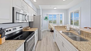 A modern kitchen with white cabinets, stainless steel appliances, granite countertops, and a view through the window. - Bonita Greens Retreat | Golf View Condo | Highland Woods | Near Bonita Beach (Bonita Springs)