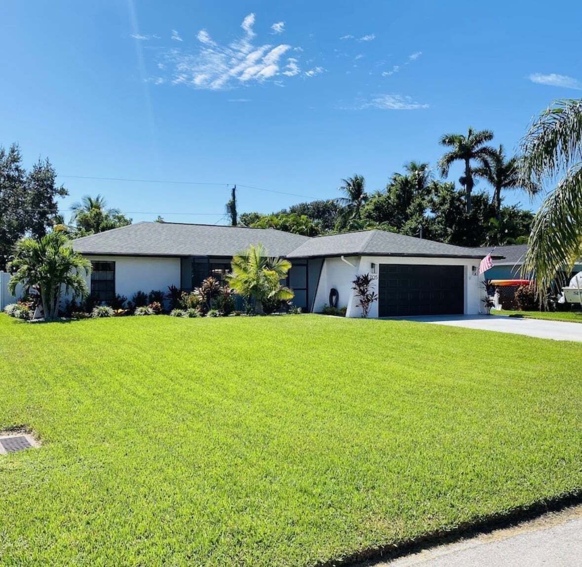 A single-story house with a garage, surrounded by a well-maintained lawn and palm trees.