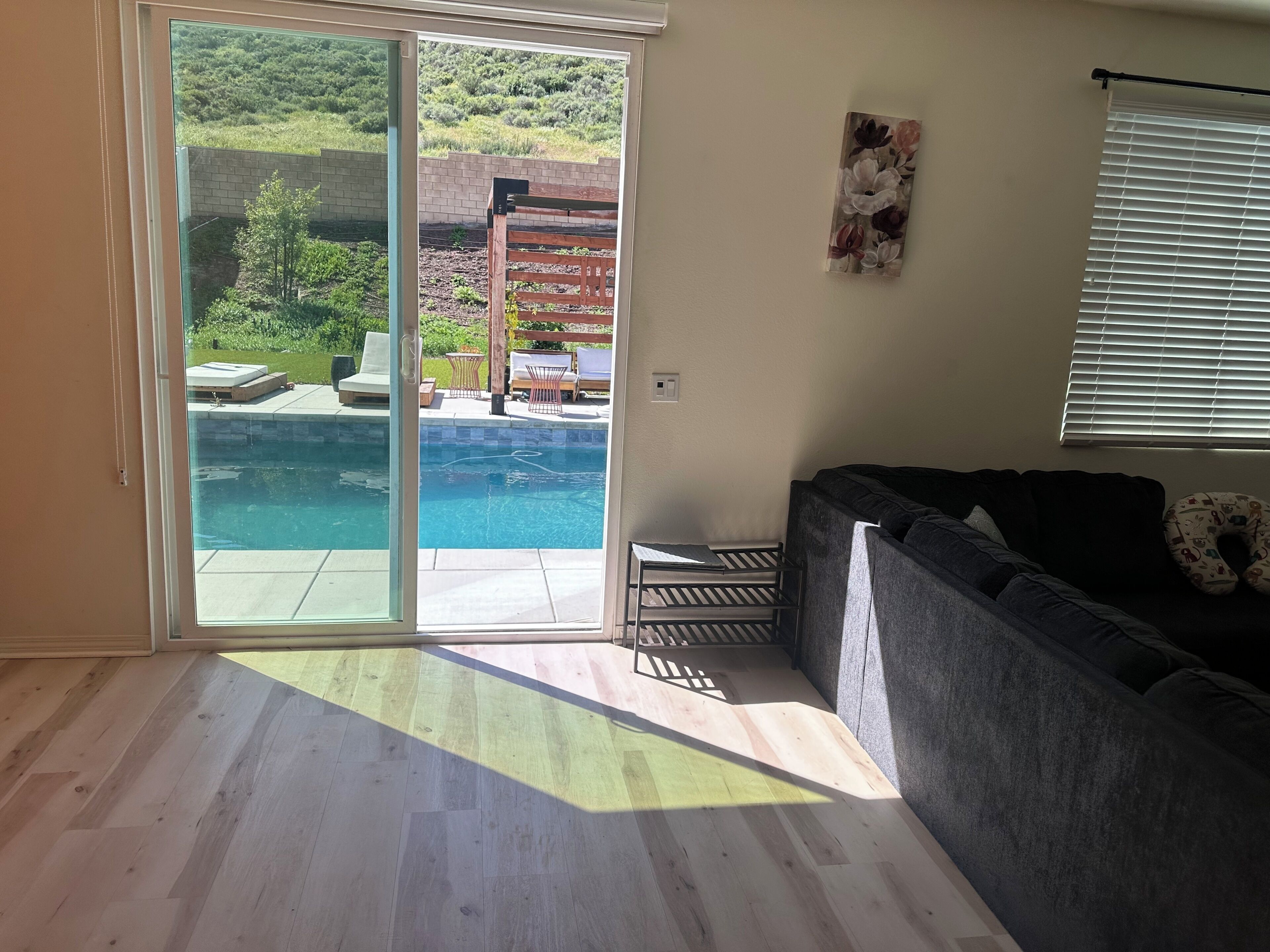 A room with a sliding glass door leading to a pool, a gray sofa, and a wall-mounted painting.