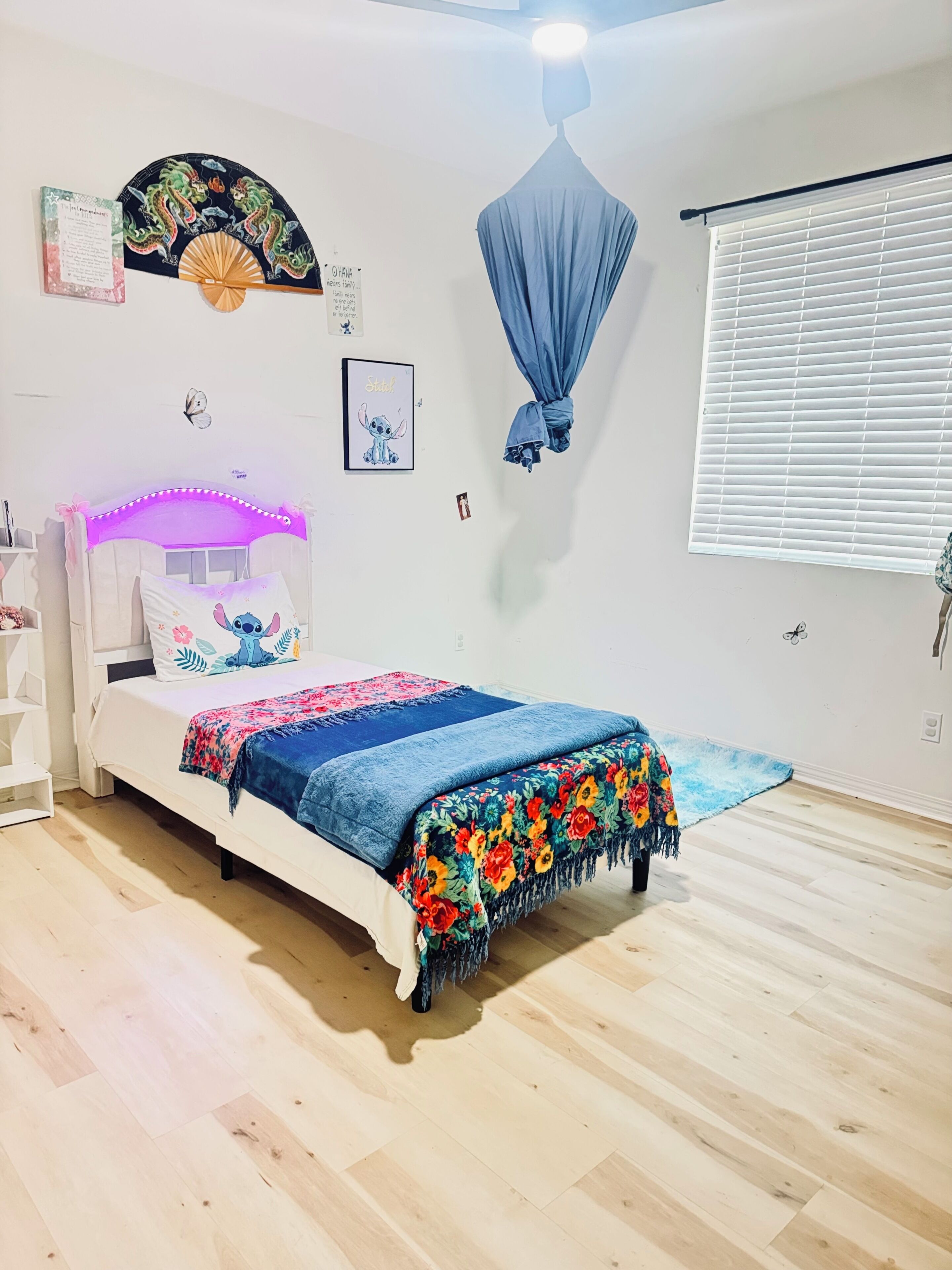 A bedroom with a bed, a ceiling fan, a window with blinds, and a wall-mounted fan.