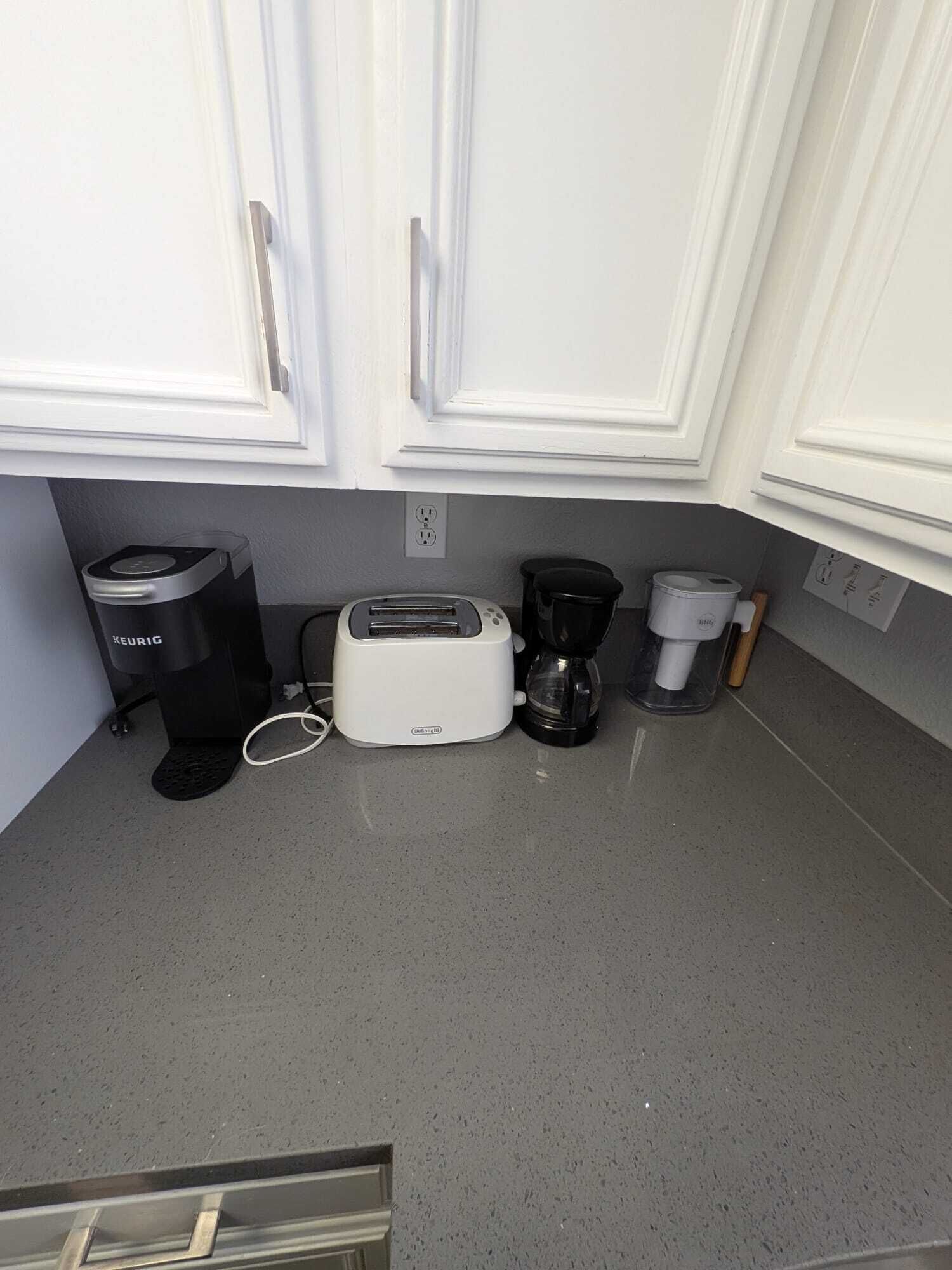 A kitchen with white cabinets, a toaster, a coffee maker, and a trash bin.