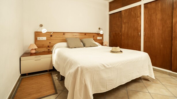 A bedroom with a wooden headboard, a bed with white bedding, a nightstand with a lamp, and a wardrobe. - Ref. CANYET : Charming House in the Heart of l’Escala with Terrace and Air Conditioning (L'Escala)