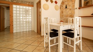 A dining area with a white table and chairs, a stone wall, and a view through a glass door. - Ref. CANYET : Charming House in the Heart of l’Escala with Terrace and Air Conditioning (L'Escala)
