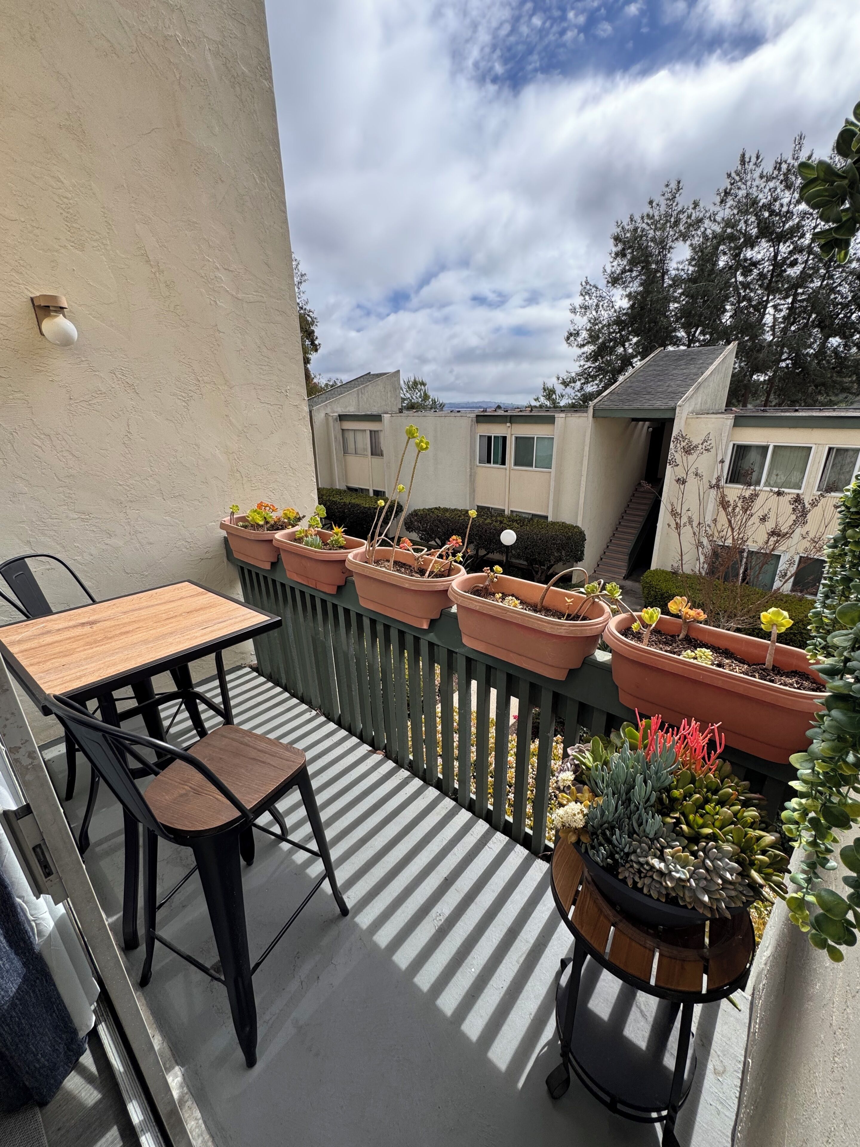 Un balcon avec une table et des chaises, entouré de plantes en pot.