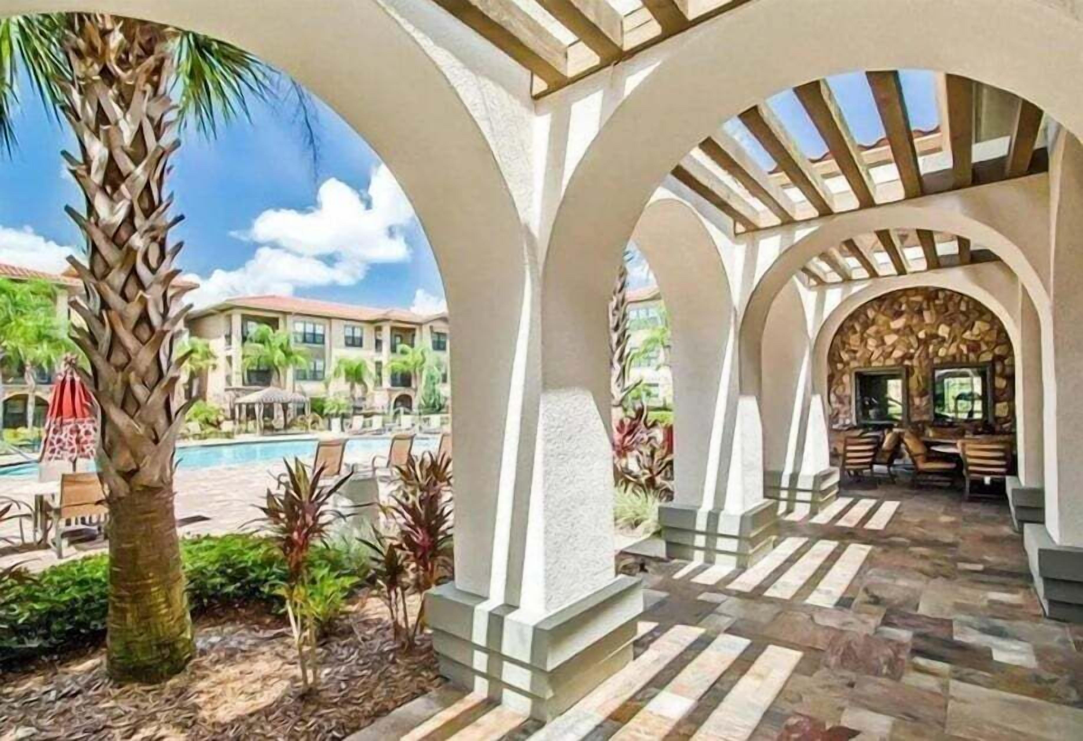 Un espacio al aire libre techado con piscina, palmeras y suelo de piedra.