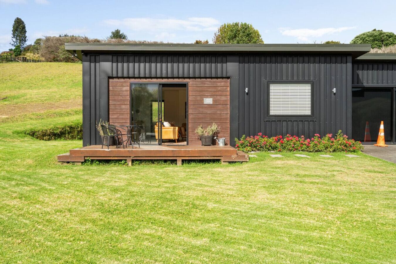 Ein modernes Gebäude mit einer Holterrasse, einer Glastür zum Durchfahren und einem kleinen Garten.
