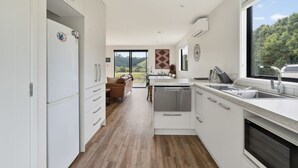 Une cuisine moderne avec des meubles blancs, un lave-vaisselle et une grande fenêtre donnant sur un paysage verdoyant.
