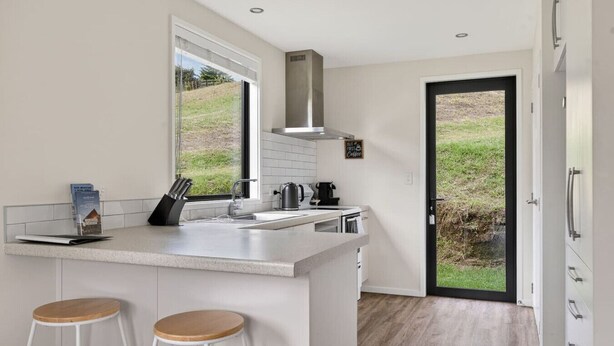 Une cuisine moderne dotée d’un grand îlot central, d’une cuisinière intégrée et offrant une vue à travers la porte.