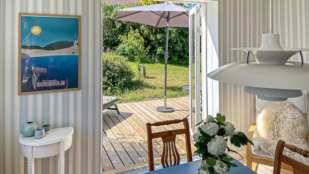 Ein Zimmer mit Blick auf einen Garten, ein Tisch mit Stühlen, eine Vase mit Blumen und ein gerahmtes Bild an der Wand.