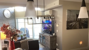 Un salon moderne comprenant un coin repas, un grand téléviseur à écran plat et une horloge murale.