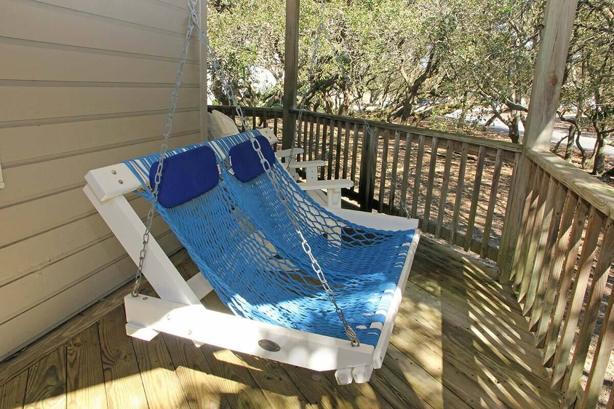 Un fauteuil suspendu, de type hamac, sur une terrasse en bois dotée d’une balustrade blanche.