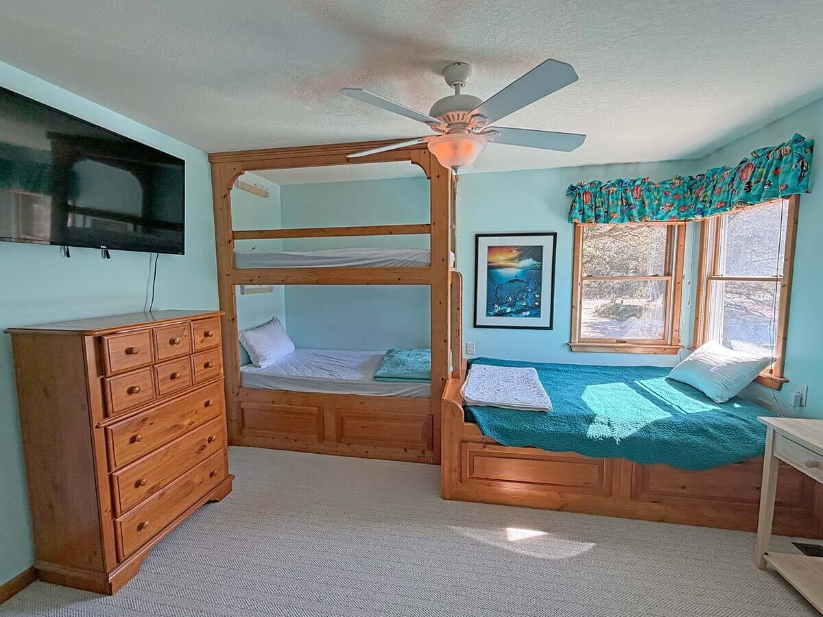 A bedroom with a bunk bed, a dresser, a ceiling fan, and a window with curtains.