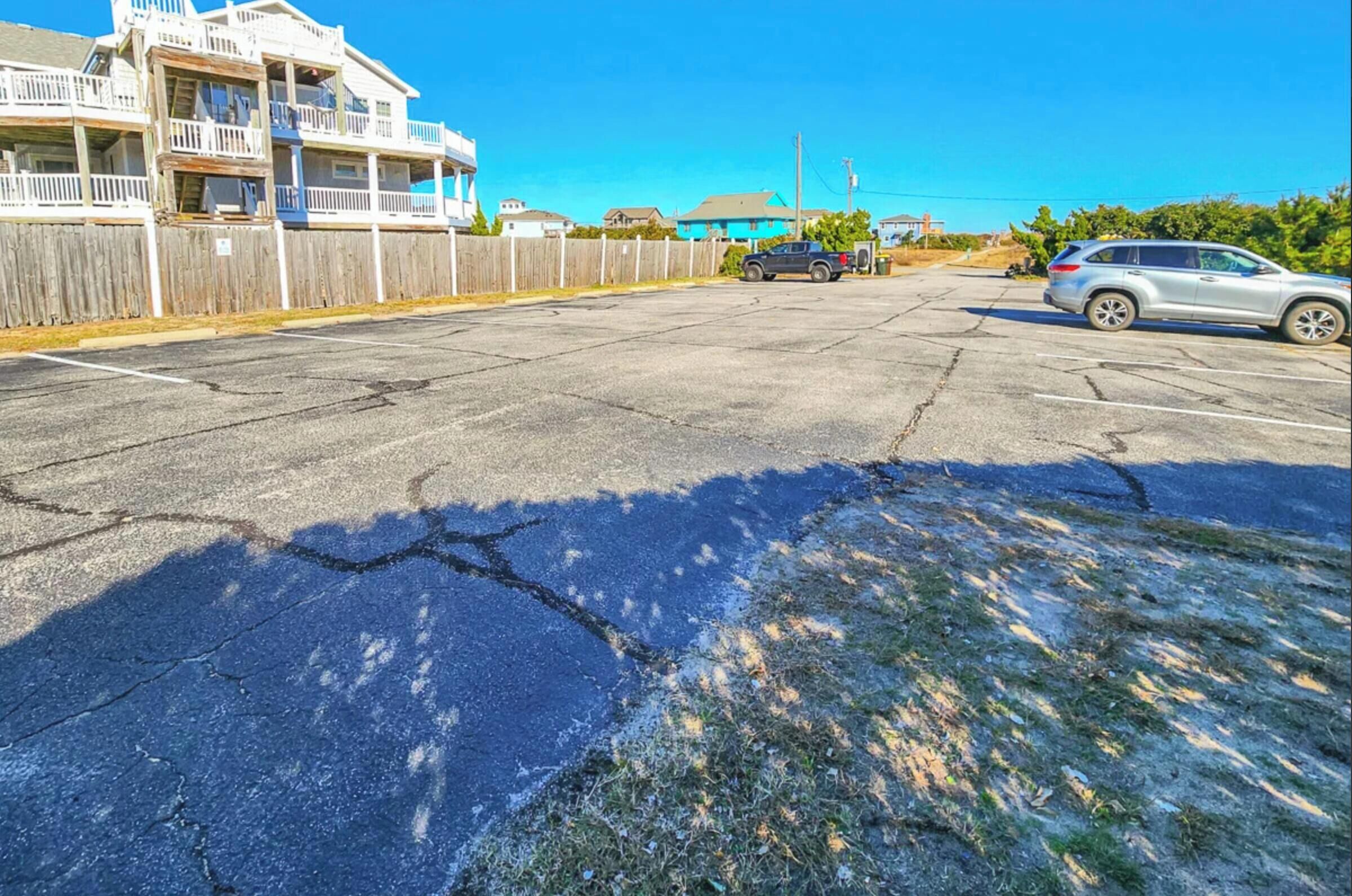 A parking lot with a damaged asphalt surface, a wooden fence, and a building with balconies.