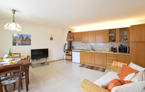 A modern kitchen with wooden cabinets, a dining area with a TV, and a living room with a sofa.