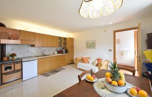A modern kitchen with wooden cabinets, a dining table with fruit, and a living area with a sofa.