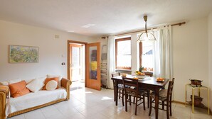 Una sala de estar con sofá, una mesa de comedor con sillas, un área de cocina y una ventana con cortinas.
