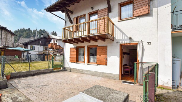 Una casa de dos pisos con balcón, patio empedrado y jardín cercado.