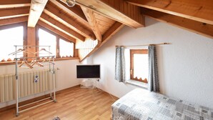 Una habitación con techo inclinado, vigas de madera, un radiador, un televisor, una cama y una ventana con cortinas.