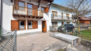 Una casa de dos pisos con un balcón, un coche estacionado en la entrada y un patio cercado.