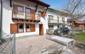 A two-story house with a balcony, a car parked in the driveway, and a fenced yard.