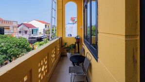 En balkon med gul væg, et lille bord med stole, en potteplante og udsigt til omkringliggende bygninger.