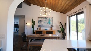Uma sala de jantar com teto de madeira, um lustre moderno, uma planta de cacto e um quadro na parede.