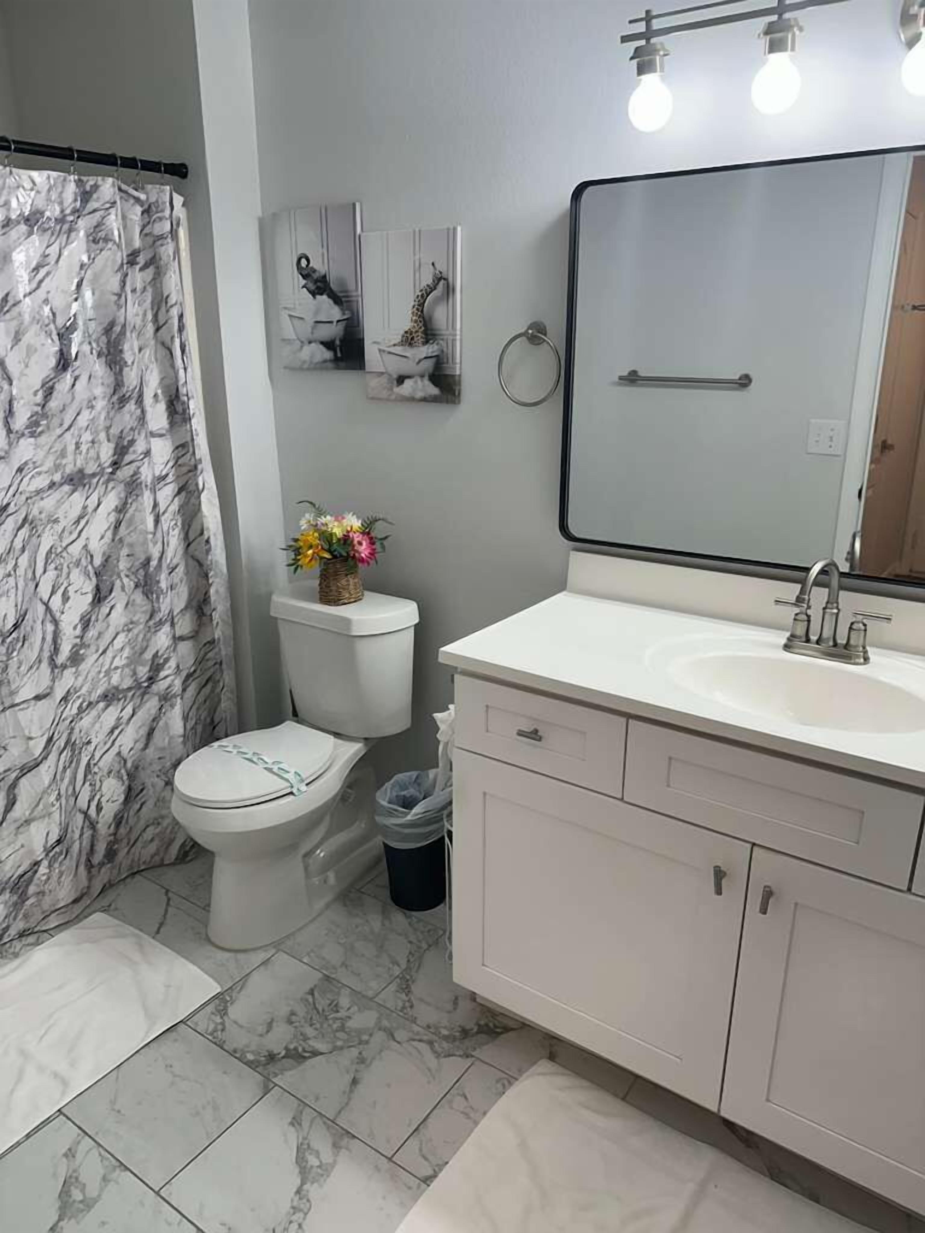 A bathroom with a toilet, sink, vanity, and a shower curtain.
