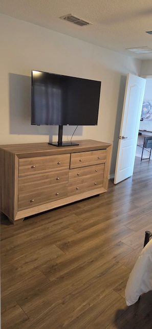 A modern living room with a flat-screen TV on a wooden cabinet, hardwood flooring, and a door leading to another room. - Spacious 4-bedroom house in awesome Davenport with AC (Davenport)