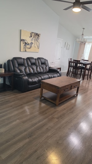 A living room with a leather sofa, a wooden coffee table, a ceiling fan, and a dining area with chairs and a table. - Spacious 4-bedroom house in awesome Davenport with AC (Davenport)