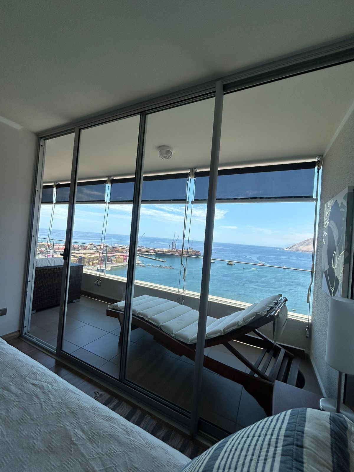 Un balcon avec vue sur la mer et le port, un lit et une chaise.