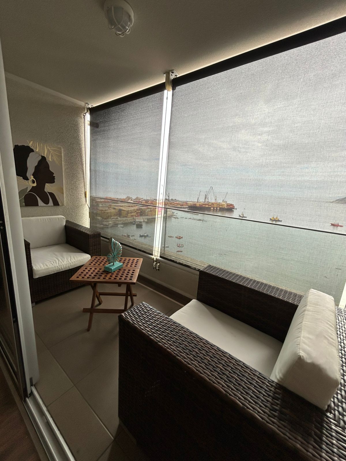 A balcony with wicker furniture, a small table, and a view of a port with ships.
