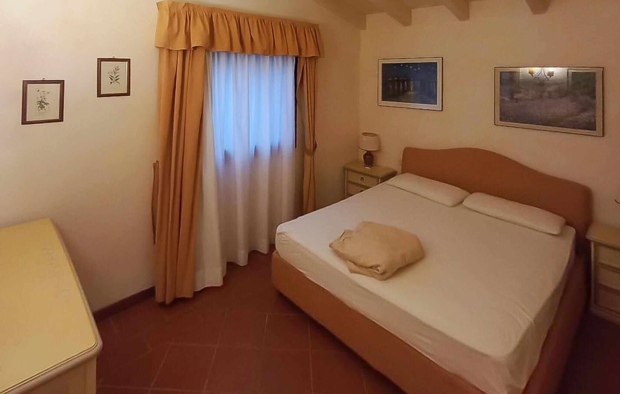 A bedroom with a bed, a nightstand, a lamp, and two framed pictures on the wall.