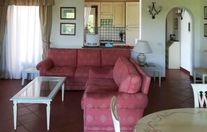 Un salon avec un canapé, une table basse en verre, un coin cuisine à l’arrière-plan et une table à manger avec des chaises.
