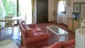 Een woonkamer met een zithoek, een glazen salontafel, een eettafel met stoelen, een witte kast en een deur.