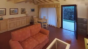 Een woonkamer met een bank, een eettafel met stoelen, een kast en een schuifpui naar een buitenruimte.