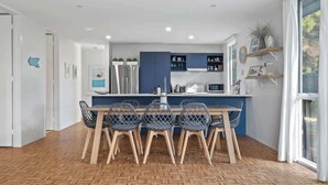 A modern kitchen with a central island, built-in appliances, and a dining area with chairs. - Sara by the sea, 400m to beach (Point Lonsdale)