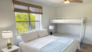 A bedroom with a bunk bed, a bedside table with a lamp, a window with a view of greenery, and a ceiling fan. - Venice Villas Paradiso - Sunny - Pool (Venice)